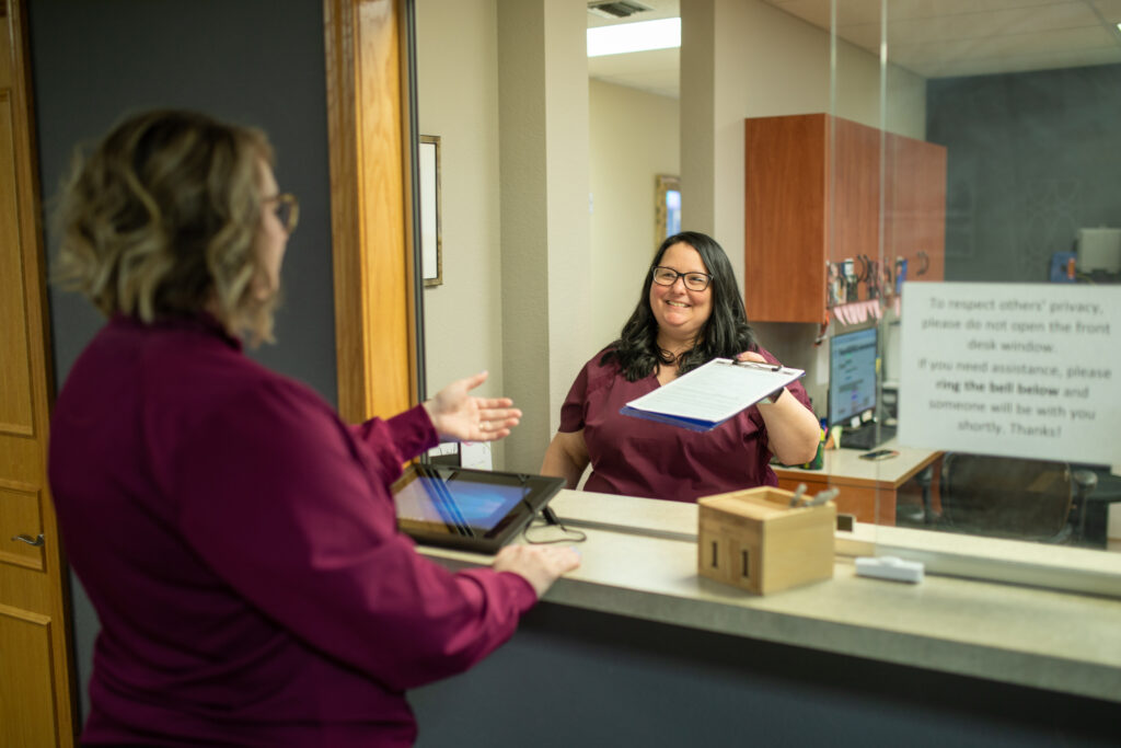 administrative assistant smiling and greeting a new patient at the front desk of Associated Oral & Implant Surgeons one of the reasons why people choose our practice