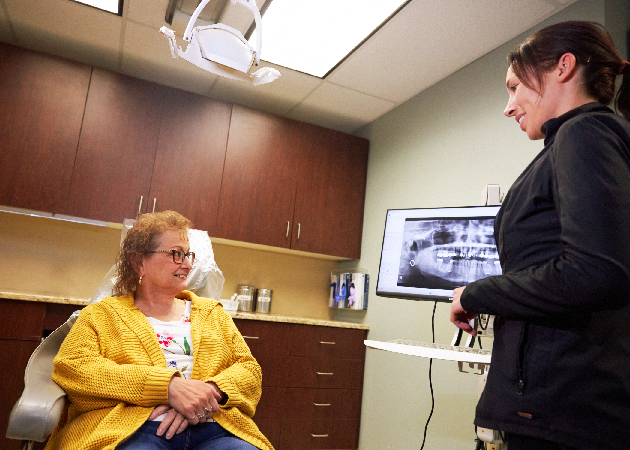 dental assistant discussing tooth extraction post operative instructions, comfort, and dentures with a patient sitting in a dental chair at Associated Oral & Implant Surgeons